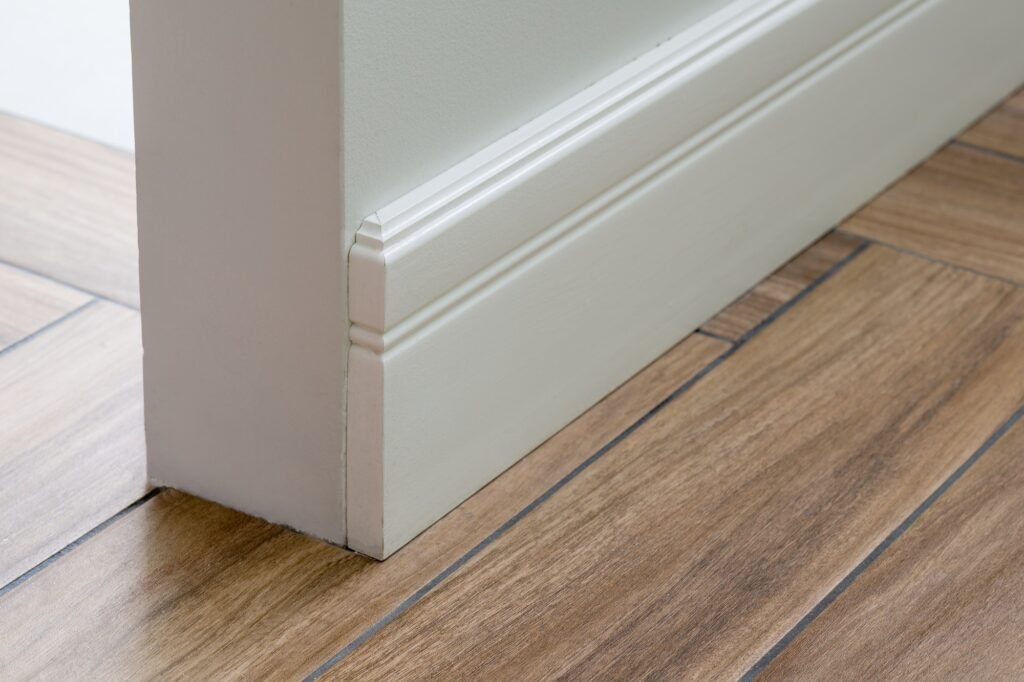 Moulding in the corner. Light matte wall with tiles immitating hardwood flooring