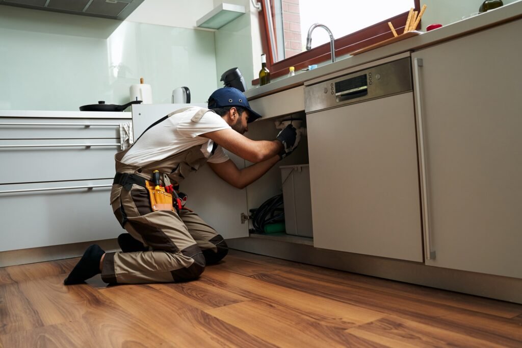 Professional male plumber in uniform is repairing a kitchen sink at home